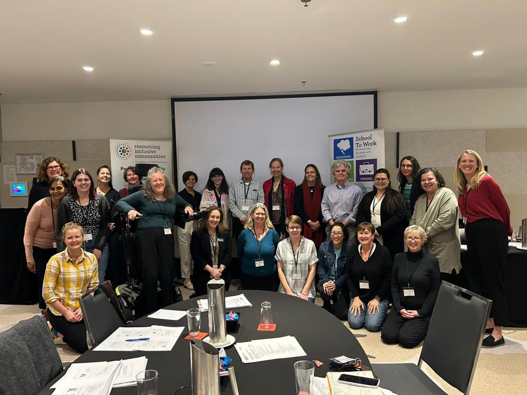 Jane standing in standing wheelchair in a big group photo in a conference room.
