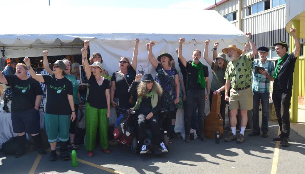 Choir in Green and black, arms raised in a power salute, standing outside a tent.